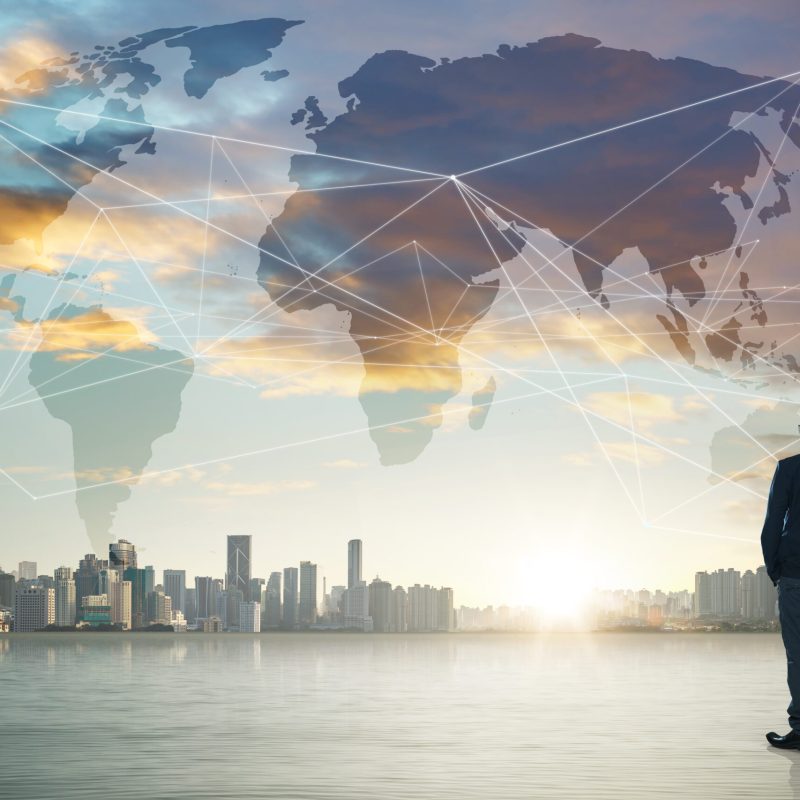 International business concept with businessman on city skyline background with network on map and sunlight